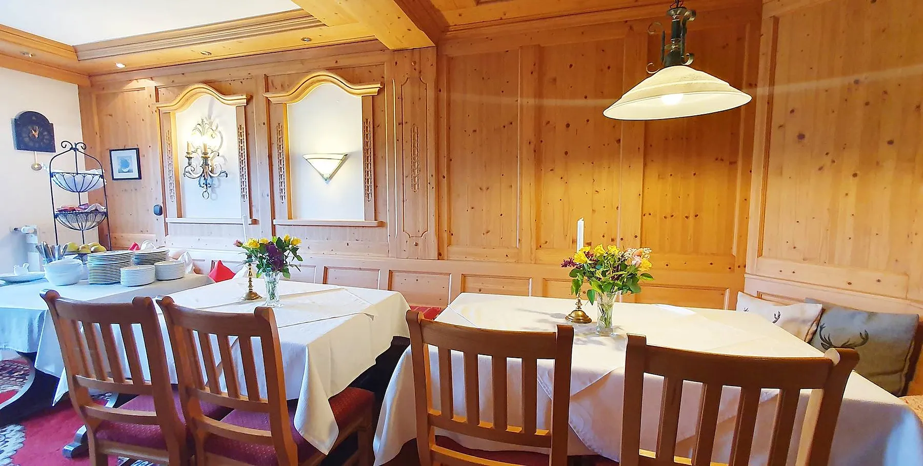 Die Frühstücksstube mit Holzvertäfelung, gedeckten Tischen und Blumen